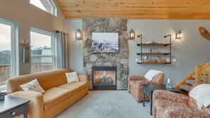 A cozy living room with a stone fireplace, wooden ceiling, and large windows. - Stunning Alaskan Getaway w/ River & Mtn Views (Eagle River)
