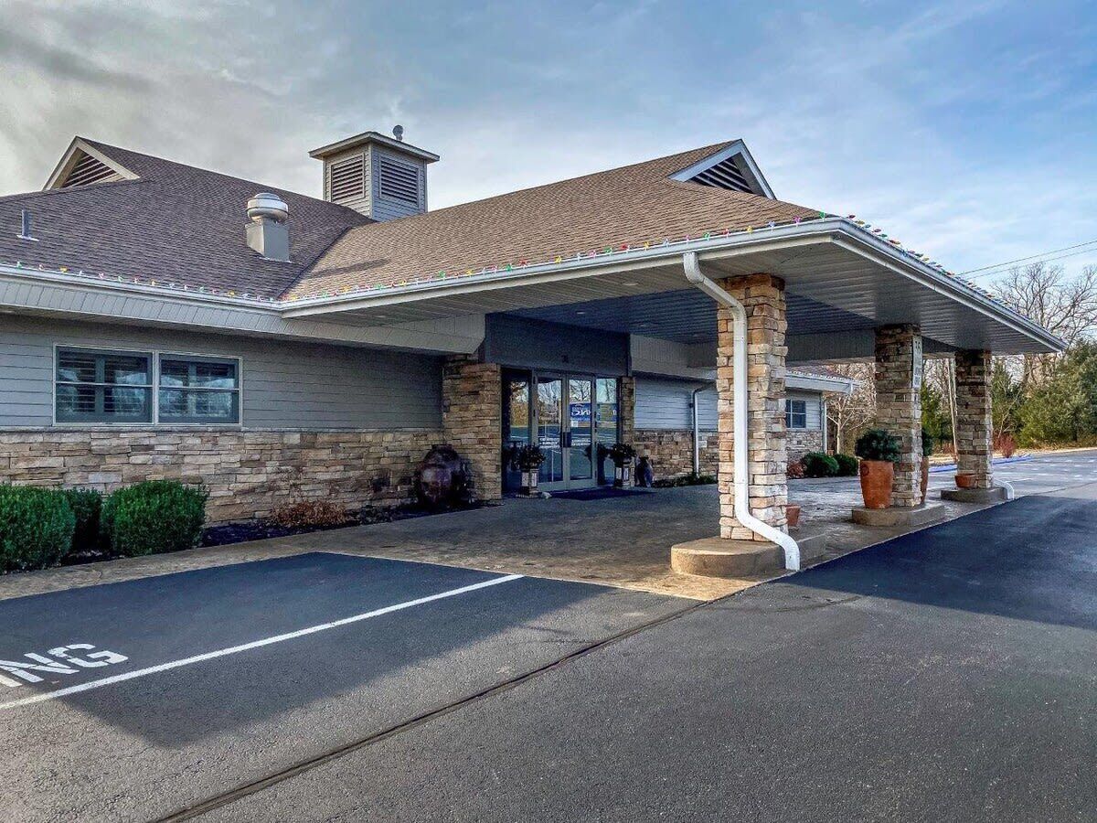 A building with a covered entrance, stone facade, and a parking lot.
