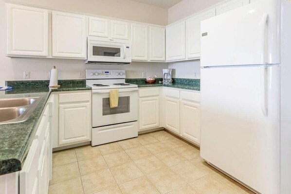 A kitchen with white cabinets, a white refrigerator, a microwave, a stove, and a coffee maker.