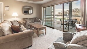 A spacious living room with a sofa set, a coffee table, and a dining area with a glass door leading to an outdoor patio. - Pool | WiFi | Lake Front | Sleeps 4 | MM 13 (491A) (Lake Ozark)