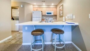 Una cocina compacta con una isla central, dos taburetes de bar y electrodomésticos modernos.