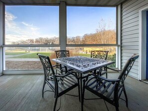 Eine überdachte Terrasse mit Tisch und Stühlen, große Fenster mit Blick auf einen Park und Gebäude.