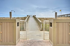 A wooden boardwalk leading to a beach area with a gate and a flag. - Sunsational Navarre Condo: Beach Chair Service (Navarre)