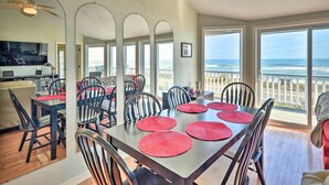 Un espace repas offrant une vue sur l’océan, avec une longue table agrémentée de sets de table rouges, de chaises noires et d’un ventilateur de plafond.