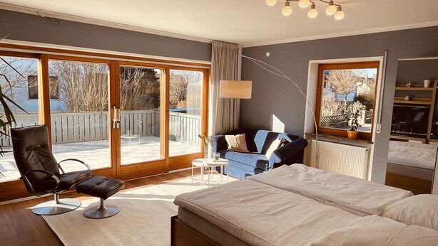 A bedroom with a large bed, a chair, a sofa, and a view of the outdoors through a sliding glass door. - mein.guesthouse - apartment 1 - approx. 45sqm with large sun terrace  (Haundorf)