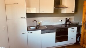 A modern kitchen with white cabinets, stainless steel appliances, and a black countertop. - mein.guesthouse - apartment 1 - approx. 45sqm with large sun terrace  (Haundorf)