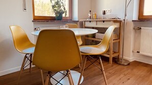 A dining area with a round table and four yellow chairs, a potted plant by the window, and a radiator on the wall. - mein.guesthouse - apartment 1 - approx. 45sqm with large sun terrace  (Haundorf)