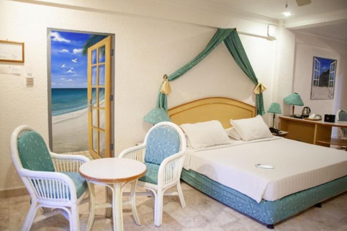 Un dormitorio con cama, dos sillas, una mesita, una mesita de noche y un cuadro de una playa.