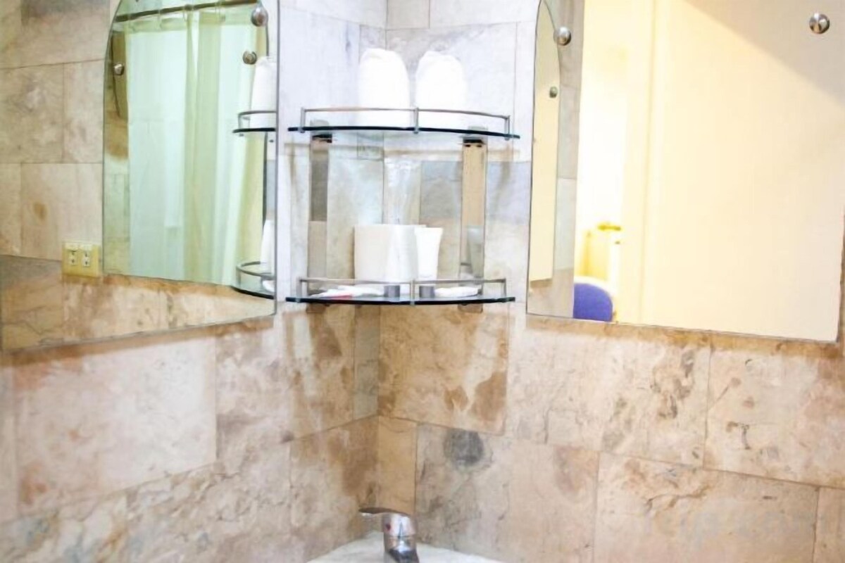 A bathroom with a marble wall, a glass soap dispenser, and a mirror.