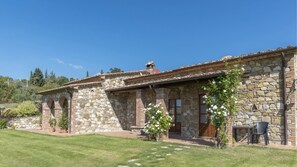 A stone building with a tiled roof, arched windows, and a small garden area with white flowers.