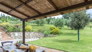 Patio esterno con muro in pietra, tavolo apparecchiato per la cena e vista su giardino curato con alberi e prato.