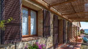 Un edificio de piedra tradicional con contraventanas de madera, un porche con tejas y flores en macetas.