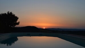 Piscina con vistas a un atardecer, rodeada de árboles y colinas.