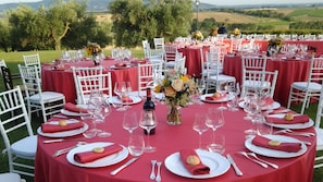 Un espace de restauration en plein air avec des tables rondes recouvertes de nappes rouges, des chaises blanches et des tables soigneusement dressées avec des verres à vin, des assiettes et des couverts.