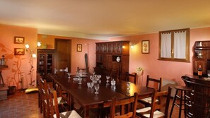 A dining room with a long wooden table set for six, surrounded by wooden chairs. There are wine glasses on the table, and a bar area with a bottle of wine and a glass. The room has wooden cabinets and a large mirror on the wall.
