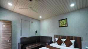 A hotel room with a bed, a bench, a wooden door, and a framed picture on the wall. - Wanderlust Resort (Akola)