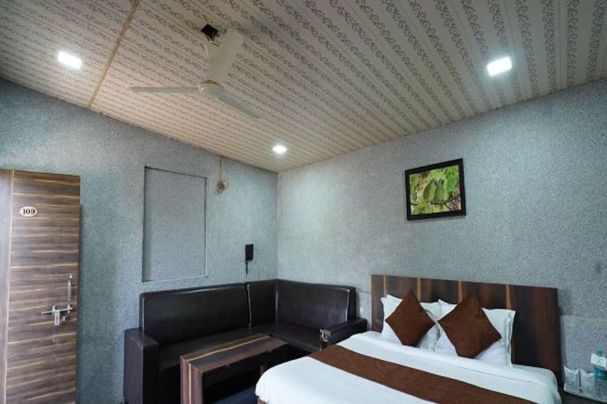 A hotel room with a bed, a bench, a wooden door, and a framed picture on the wall.