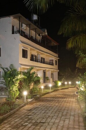 A two-story building with a balcony on the upper floor, surrounded by palm trees and a paved pathway.