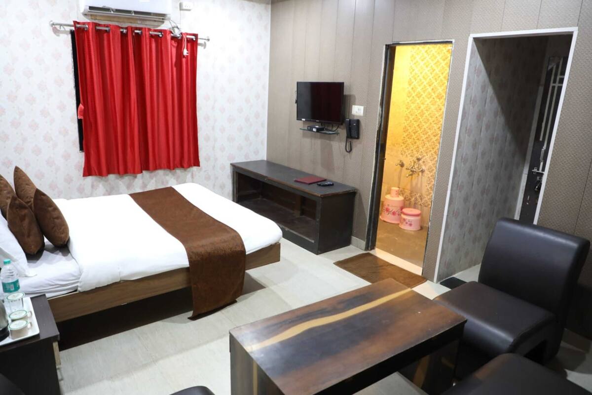 A hotel room with a bed, bedside table, TV, and a bathroom visible through a partition.
