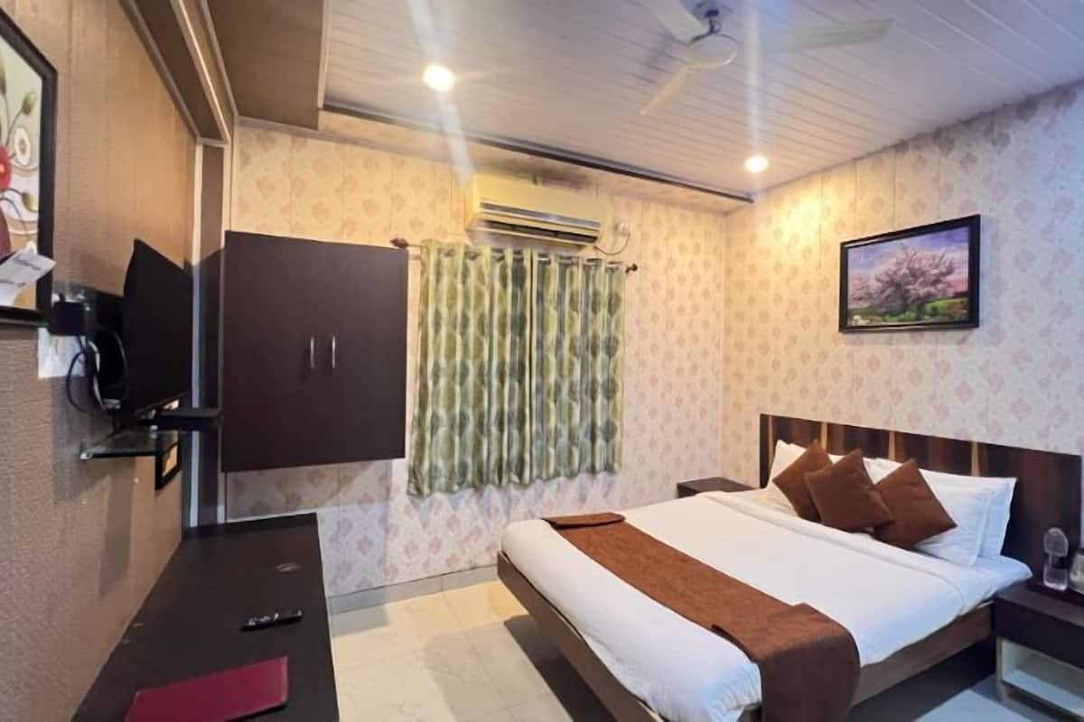 A hotel room with a bed, a desk, a TV, an air conditioning unit, and a painting on the wall.