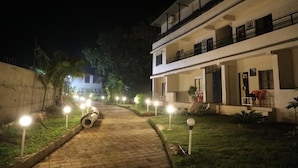 A multi-story building with a paved pathway leading to the entrance, surrounded by greenery and illuminated by ground lights. - Wanderlust Resort (Akola)