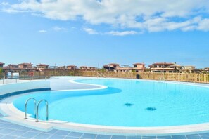 A swimming pool with a wavy edge, surrounded by a wooden fence and buildings in the background.