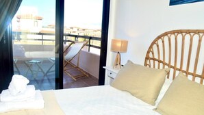 Quarto de hotel com cama, mesa de cabeceira, luminária e vista para a varanda e prédios externos.