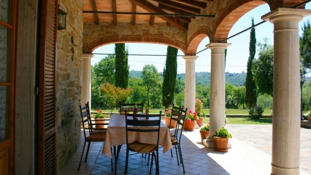 An outdoor patio with a table and chairs, surrounded by stone columns and potted plants.