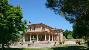 A two-story stone house with a tiled roof, a fountain, and a well-maintained garden.