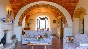 A spacious living room with a high arched brick ceiling, a fireplace, floral-patterned sofas, and a wooden coffee table.