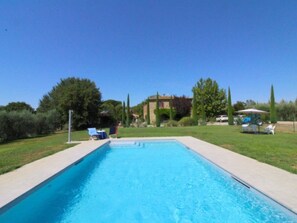 Une piscine rectangulaire à l’eau d’un bleu limpide, entourée d’une terrasse en béton. On y trouve des chaises longues et une petite table, toutes deux protégées par des parasols.