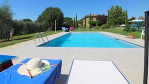 Une piscine avec des chaises longues et une table sur laquelle se trouvent un chapeau et un livre.