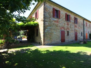 Un bâtiment en pierre avec des volets rouges, une entrée abritée et une pelouse bien entretenue.