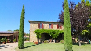 Un bâtiment en pierre avec des volets rouges, une pelouse bien entretenue et deux arbres hauts et élancés.