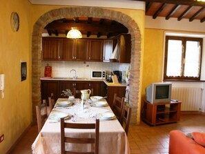 A dining area with a table set for four, a kitchen with wooden cabinets, a microwave, and a television in a corner.