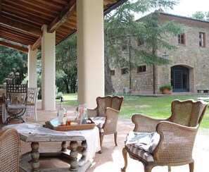 Eine Terrasse im Freien mit Korbmöbeln, einem Tisch mit weißer Tischdecke und einem Steinhaus im Hintergrund.