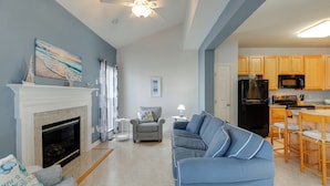 A living room with a fireplace, a sofa, and a kitchen area with wooden cabinets and a refrigerator. - < 3 Mi to Bethany Beach: Family Gem w/ Game Room (Millville)