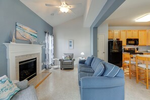 A living room with a fireplace, a sofa, a dining area with a table and chairs, and a kitchen with wooden cabinets and appliances.