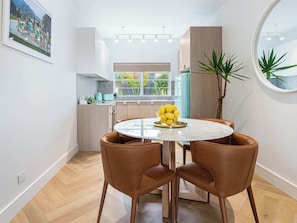 A modern kitchen with a dining area, a window with a view of greenery, and a small plant on the counter.