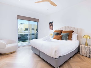A modern bedroom with a large bed, a chair, a lamp, and a view through a glass door.