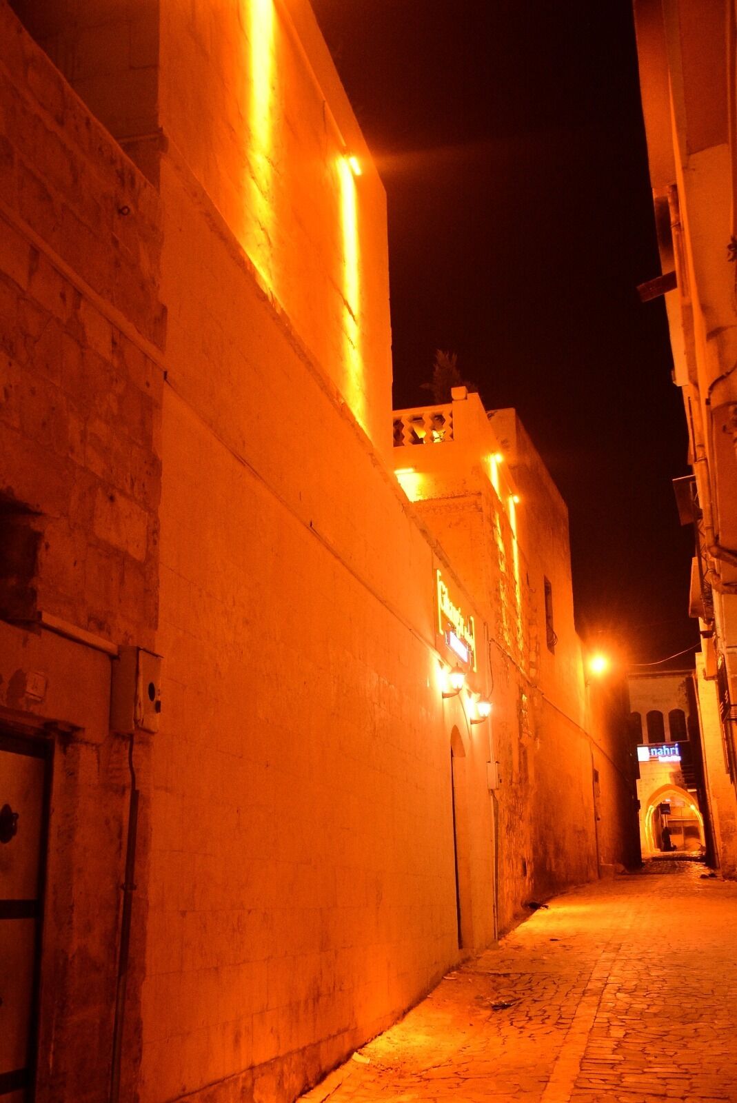 Eine schmale Straße bei Nacht, gesäumt von Gebäuden, die warm beleuchtet sind.