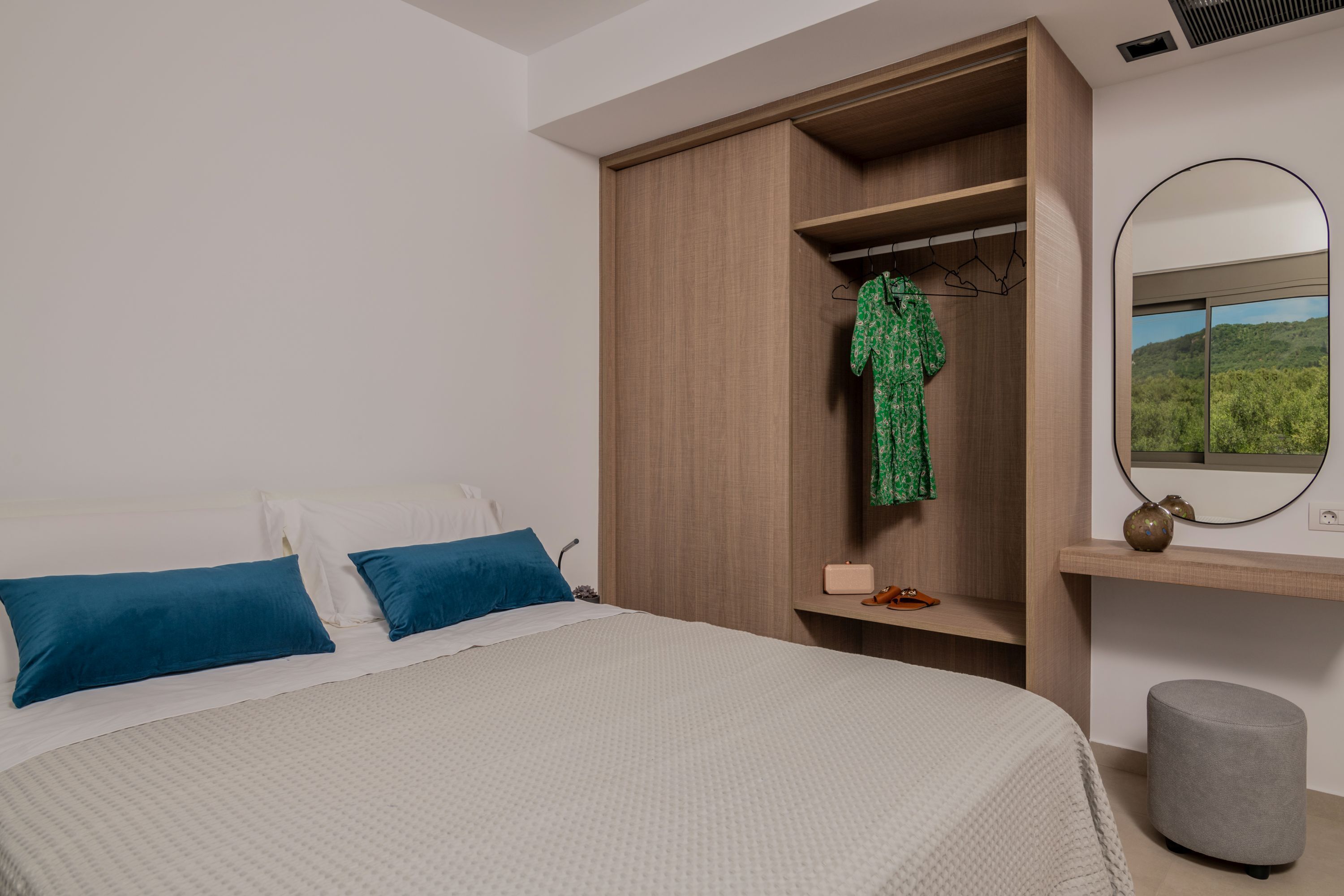 Een slaapkamer met een bed, een kledingkast, een spiegel en uitzicht op groen.