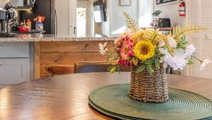 A dining table with a woven basket containing flowers, a green placemat, and a wooden chair. - DT Bar Harbor,2 King beds & Decks, Parks 3 small cars, Town Pickleball Ct @ Back (Bar Harbor)