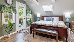 A bedroom with a large bed, two bedside lamps, a bench, a clock, and a view of the outdoors. - DT Bar Harbor,2 King beds & Decks, Parks 3 small cars, Town Pickleball Ct @ Back (Bar Harbor)