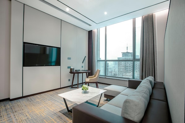 Una habitación de hotel moderna con un ventanal grande, un televisor de pantalla plana, un sofá, una mesa de centro y un pequeño escritorio con una silla.