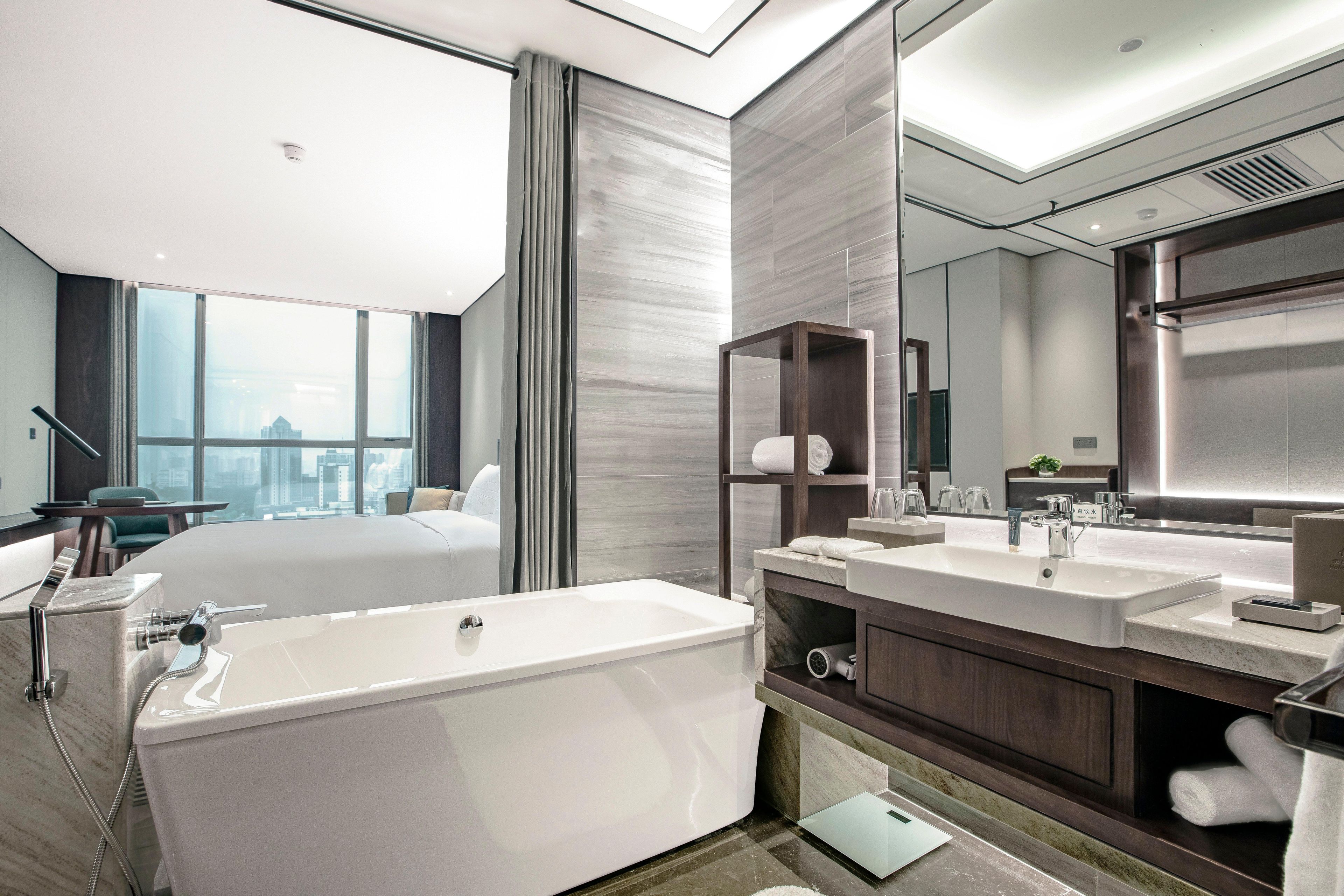 Ein modernes Hotelzimmer mit einer großen Badewanne, einem Doppelbett, einem großen Fenster und Blick auf die Stadt.