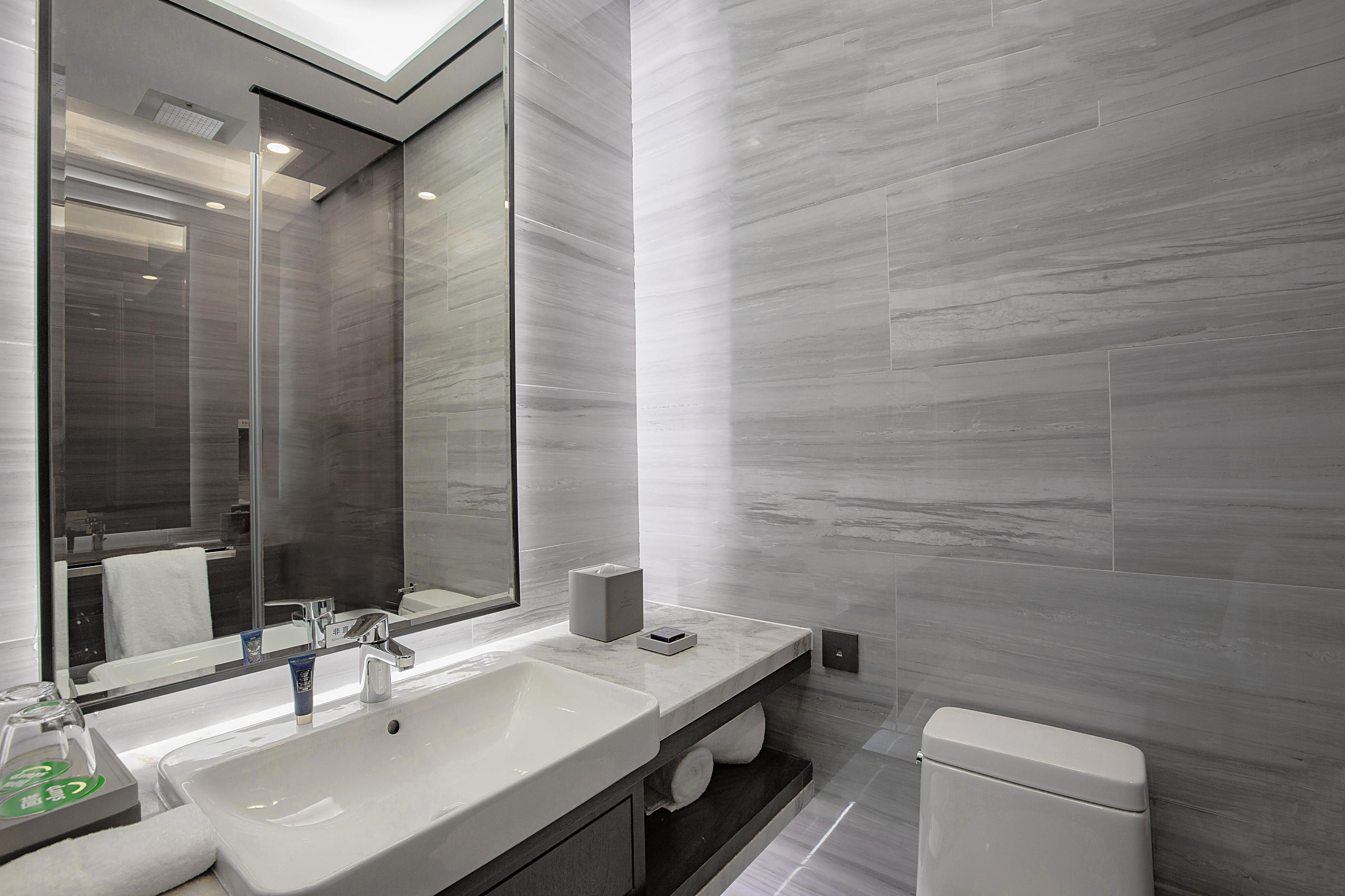 A modern bathroom with a large mirror, a sink, a toilet, and a towel rack.
