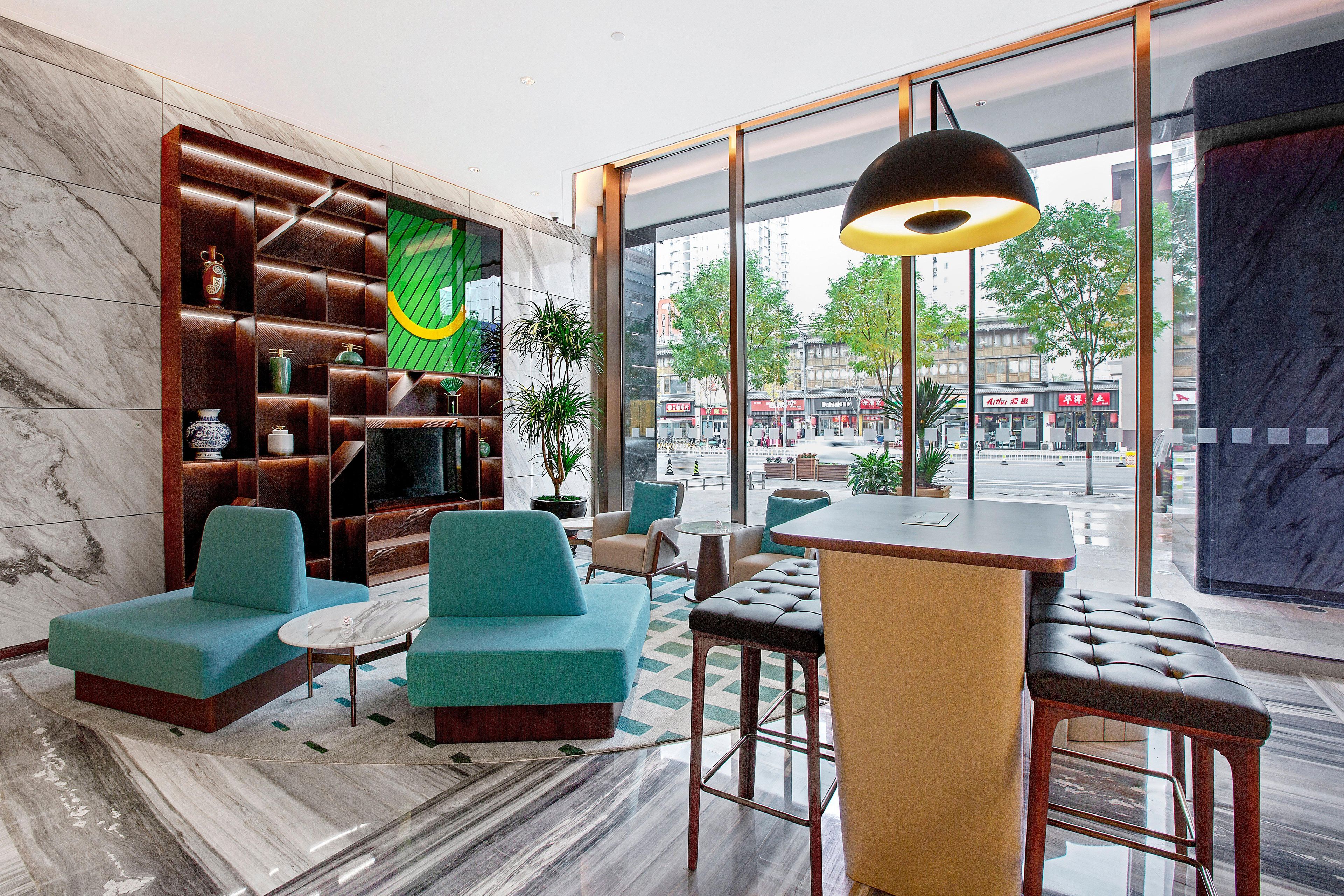 A modern lobby with seating, a bar area, and a large window offering a city view.