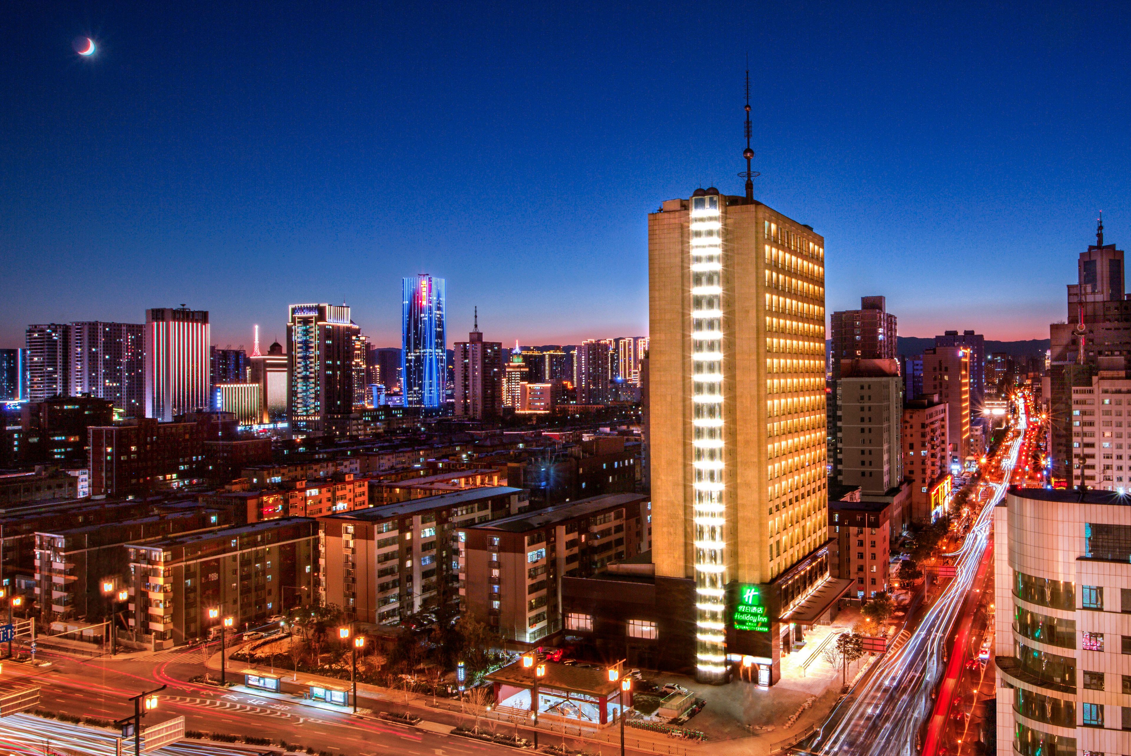 A cityscape at night with illuminated buildings and a prominent hotel with a vertical light strip.