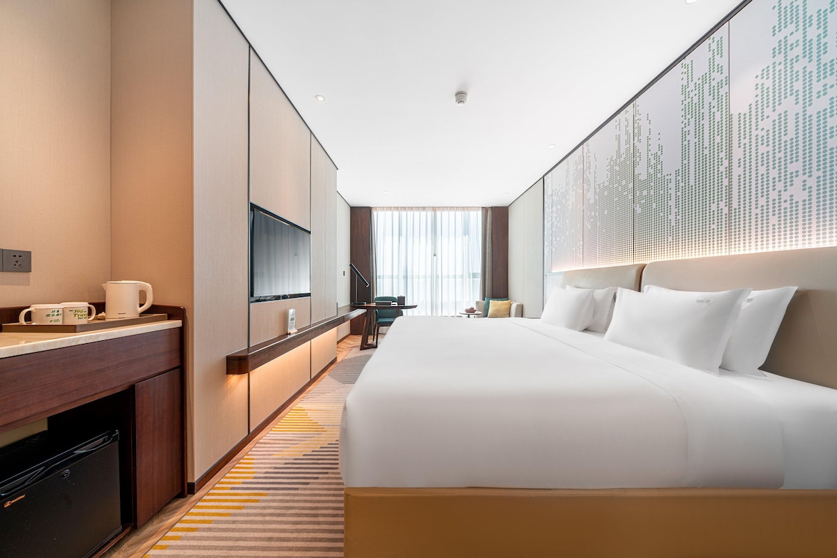 A hotel room with a large bed, a flat-screen TV, a desk with a chair, a small table, and a sofa.
